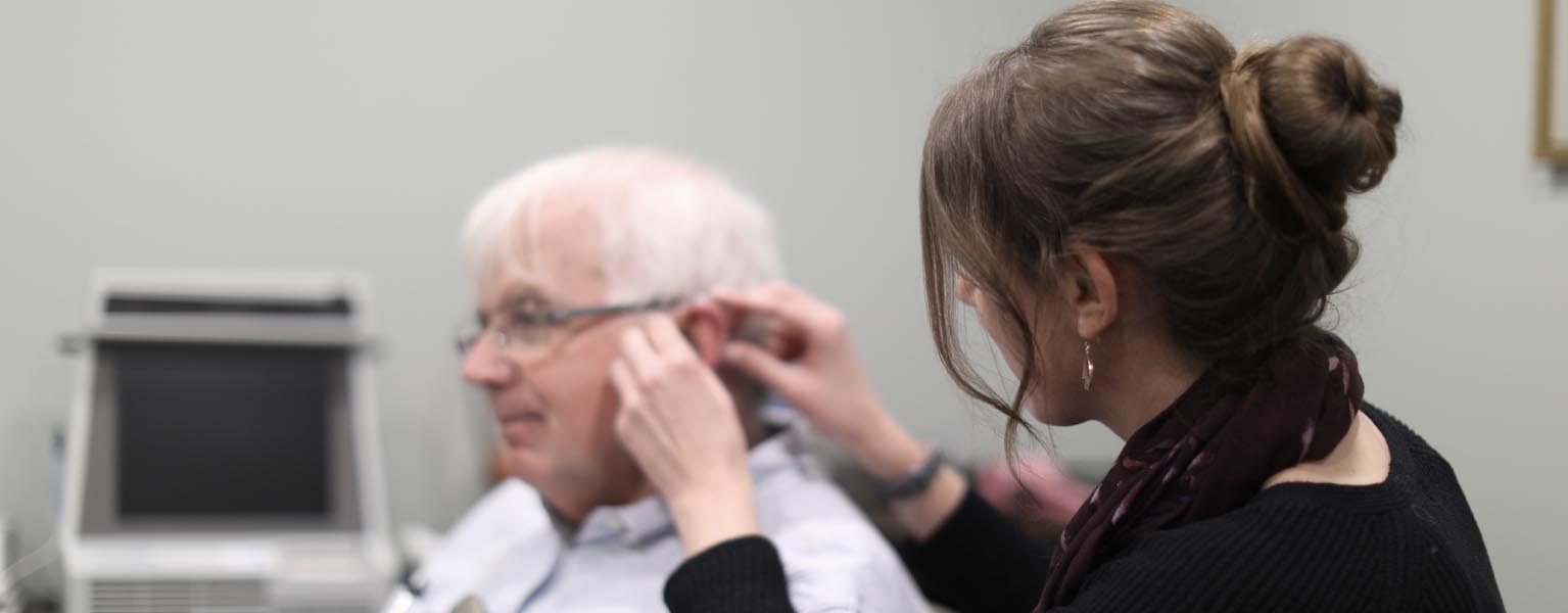 Audiologist Kelsey Meagher inserting a BTE hearing aid in a man's ear